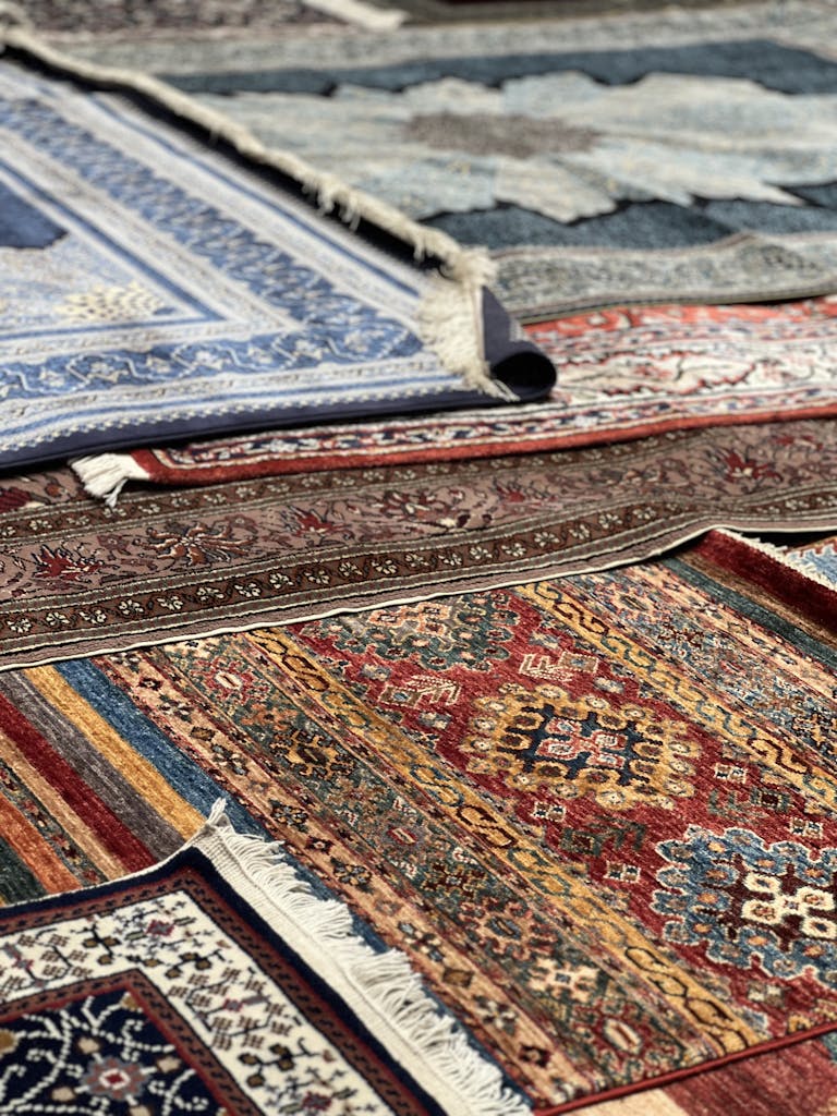living room carpet, Vibrant collection of traditional rugs and carpets displayed outdoors, showcasing intricate patterns.